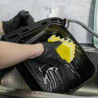 Close-up view of hands in black gloves scrubbing a dirty oven pan, demonstrating effective cleaning techniques and the importance of maintaining kitchen cleanliness and hygiene