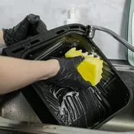 Close-up view of hands in black gloves scrubbing a dirty oven pan, demonstrating effective cleaning techniques and the importance of maintaining kitchen cleanliness and hygiene