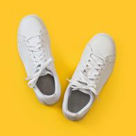 A pair of white sneakers on a yellow background in a top view