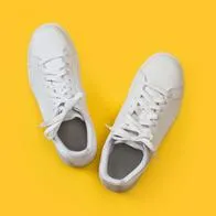 A pair of white sneakers on a yellow background in a top view