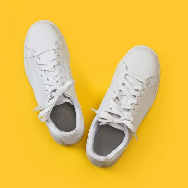 A pair of white sneakers on a yellow background in a top view