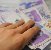 A hand adding some money to a Colombian pesos background