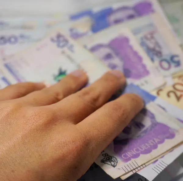 A hand adding some money to a Colombian pesos background