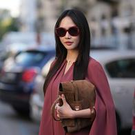 MILAN, ITALY - SEPTEMBER 24: Christinna Kuan wears long straight dark brown hair with a center part, burgundy round sunglasses with dark lenses, a burgundy oversized cape-sleeve mini dress, a brown suede leather clutch bag, outside Max Mara, during Milan Fashion Week - Womenswear Spring/Summer 2027, on September 24, 2026 in Milan, Italy (Photo by Edward Berthelot/Getty Images)