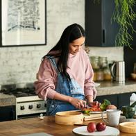 Mid adult woman chopping ingredients for meal, standing behind kitchen worktop, concentration, precision, cutting