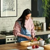 Mid adult woman chopping ingredients for meal, standing behind kitchen worktop, concentration, precision, cutting