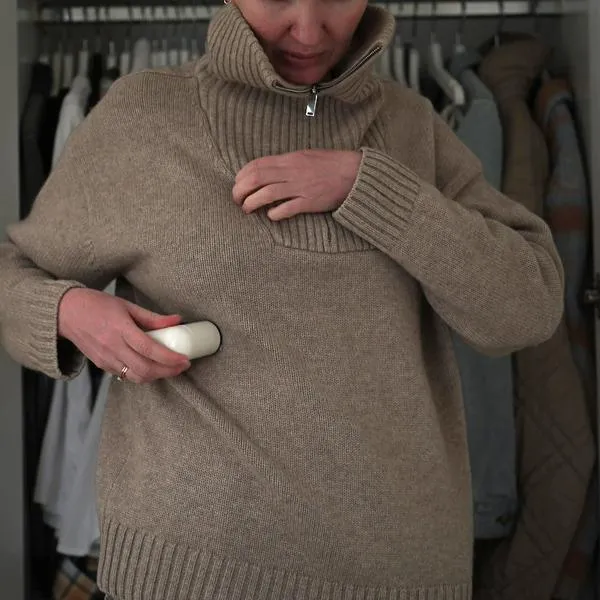 Woman removing fabric pills from beige sweater with electric lint remover at home