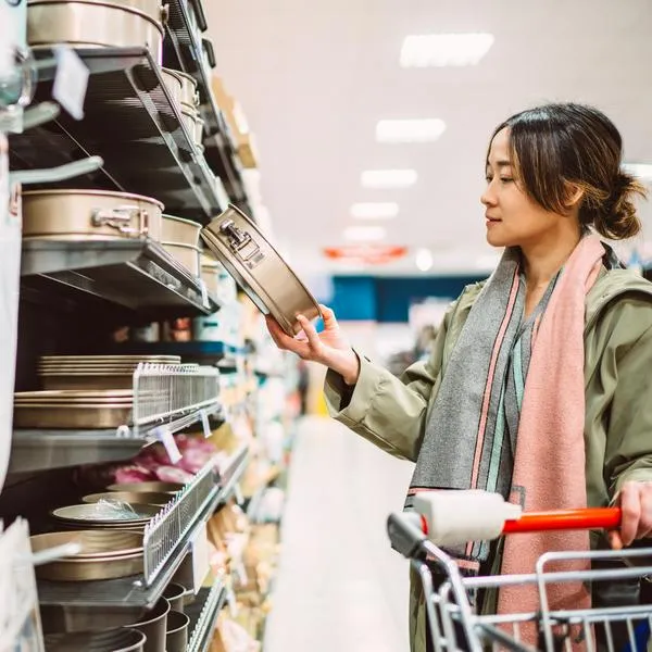 Woman comparing baking tins and kitchenware in a retail store while shopping for home essentials. Concept of consumer choice, home cooking lifestyle, and everyday shopping decisions.