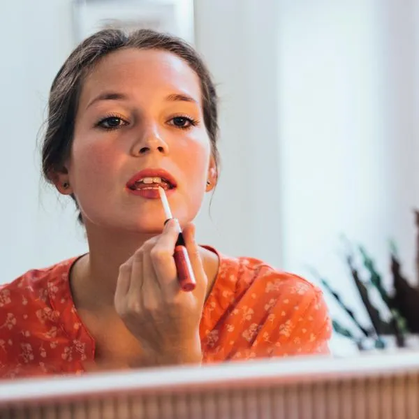 Woman applying lipstick in front of a big mirror.