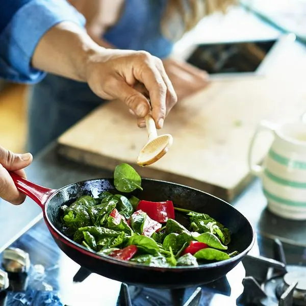 Close up of man holding frying pan with fresh vegetables and wooden spoon