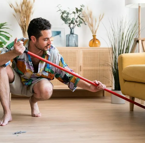 Man cleaning the floor of the living room of his house with a broom.