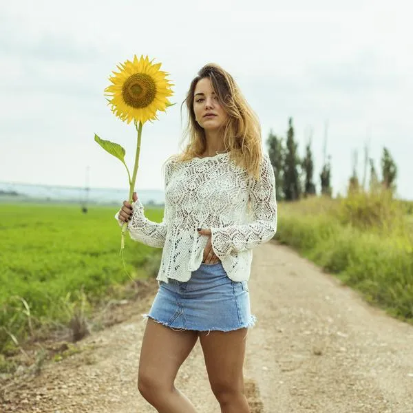 Young woman on a dirt road holding a sunflower