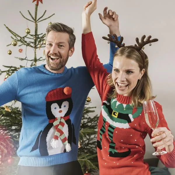 Two people with ugly Christmas sweaters dancing in front of tree