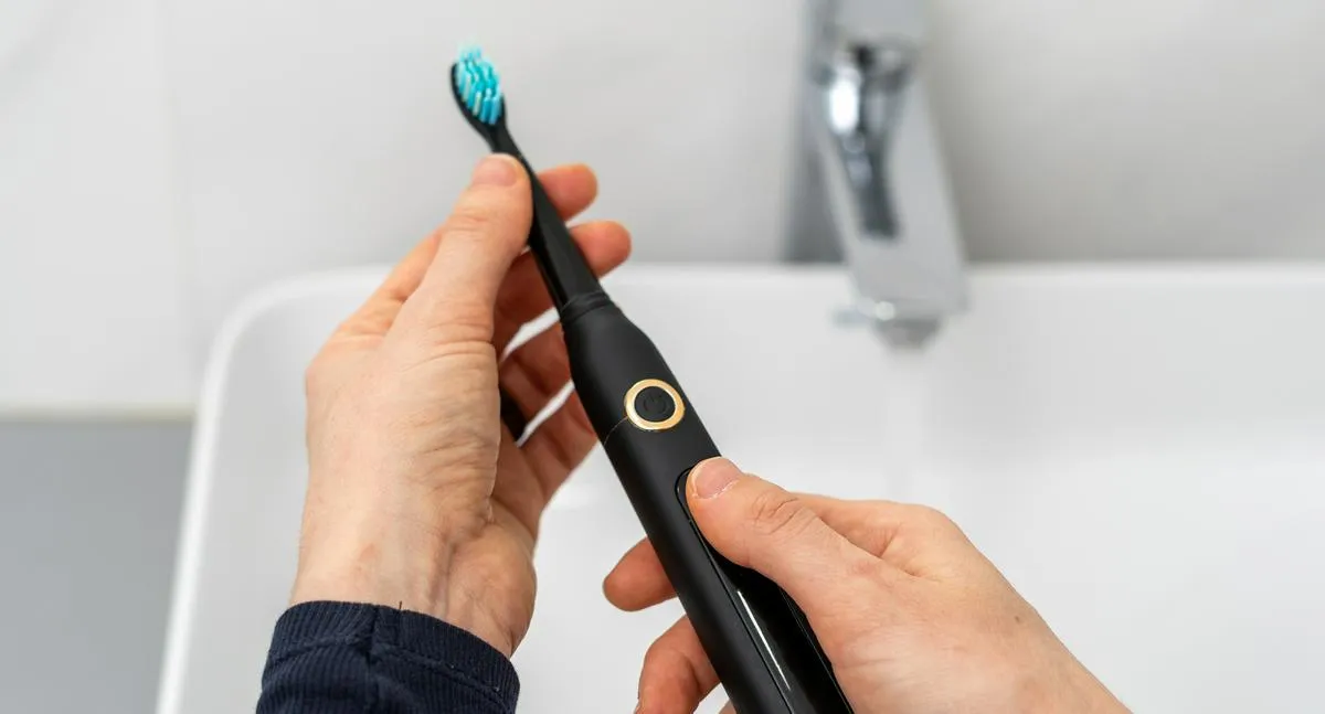 Pov woman hold professional sonic electric toothbrush with replaceable brush in hands over sink on blurred background. Wireless equipment and oral care concept