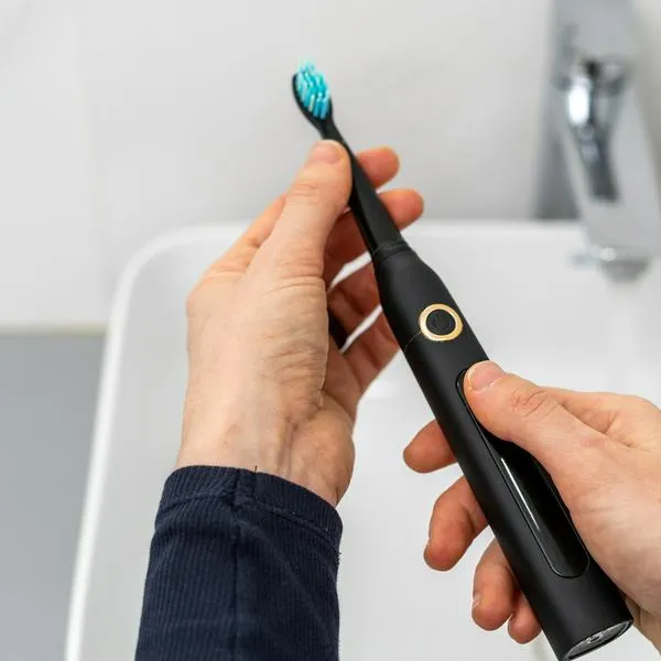 Pov woman hold professional sonic electric toothbrush with replaceable brush in hands over sink on blurred background. Wireless equipment and oral care concept