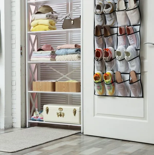 Organizer with different footwear on door, accessories and clothes indoors. Shoe storage