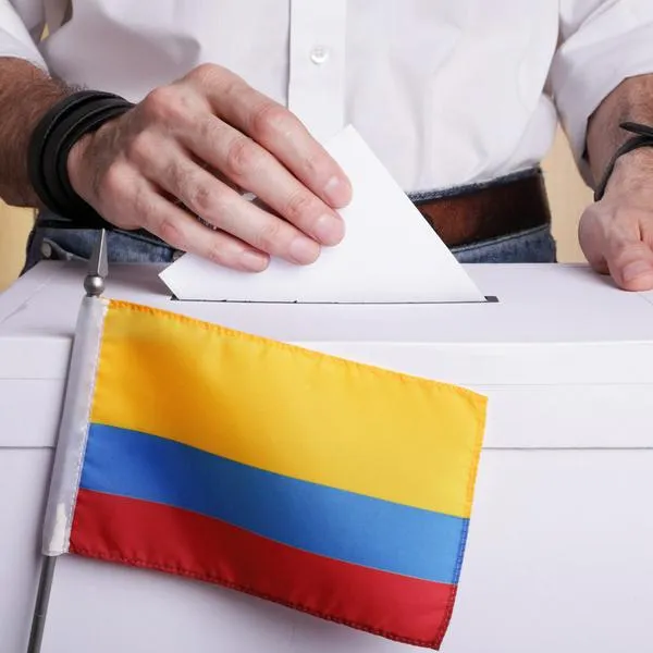 A man inserting a ballot to a ballot box.  Colombian flag in front of it.
