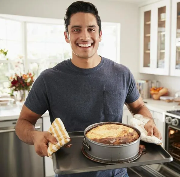 Smiling millennial Hispanic man standing in kitchen presenting the cake he has baked to camera