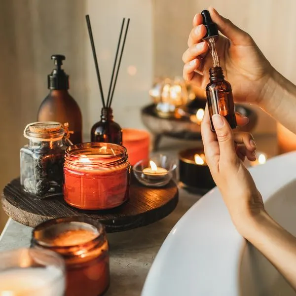 Female hands holding pipette with organic oil in hand, applying serum on fingers, on the background of a bath with candles. Protector skin treatment, facial essence oil, Vitamin C. Beauty and spa concept. Anti-stress and detox procedure.
