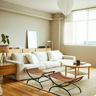 Sofa with coffee table by window in living room. Folding portable stool is kept on carpet at home. Interior of modern bright apartment.