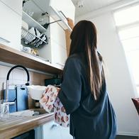 Woman putting away clean dishes into a kitchen cabinet, engaging in daily household chores and maintaining a tidy home