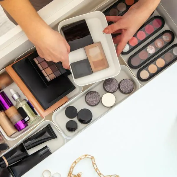 Woman hands neatly organizing makeup or cosmetics in the drawer of vanity dressing table and leaving her jewellery on dressing table surface. Visagiste is taking out vanity case of cosmetic powders