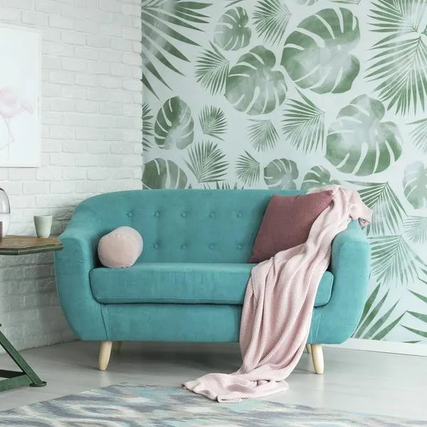 Green table with plant between pink chair and blue sofa in floral living room with wallpaper and poster