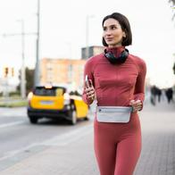 Woman jogging on a city street, carrying a smartphone and wearing headphones