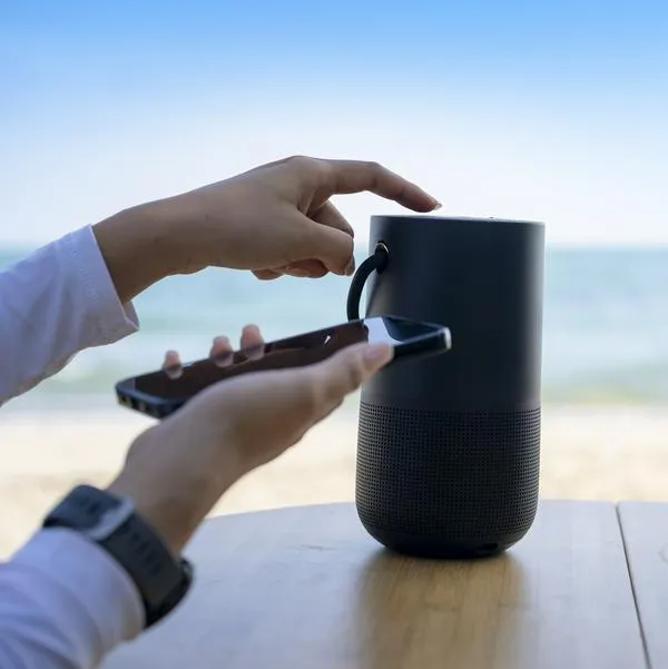 Hands connecting cell phone with bluetooth speaker with beach background, Vacation activity.